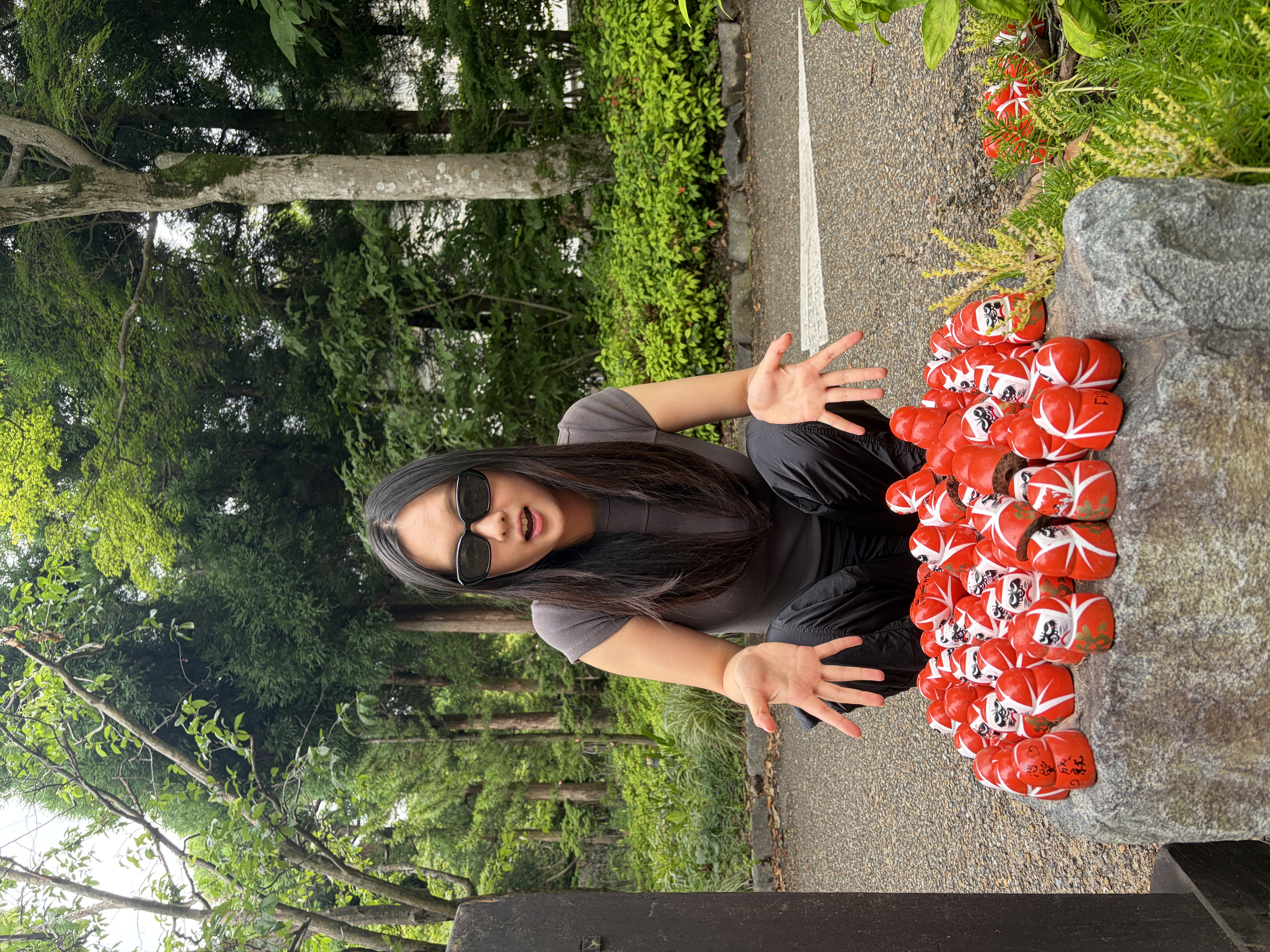 Brenda sitting beside red daruma dolls in a garden